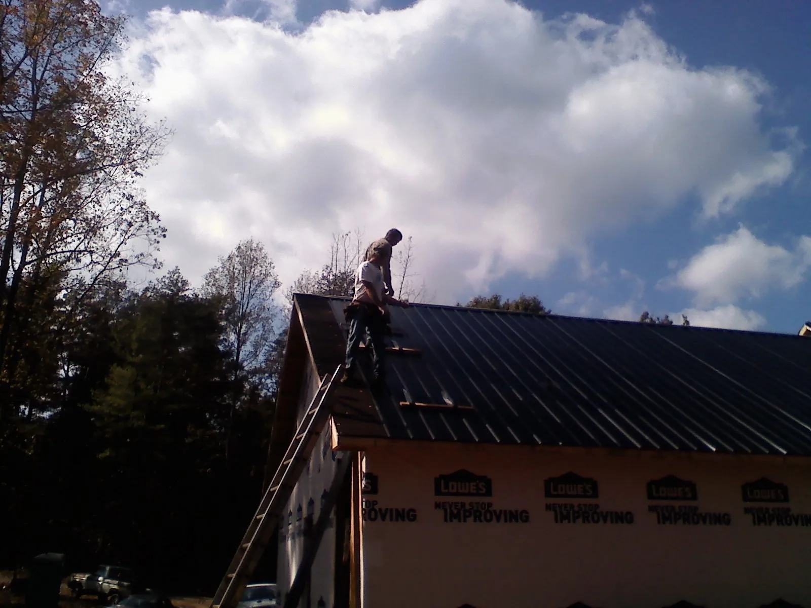 Roofer fastening dark metal panels high against a cloudy sky, from a Roof Inspection job in Kinston